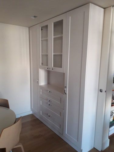Un armario blanco con puertas de cristal y cajones en una habitación con una mesa y sillas.