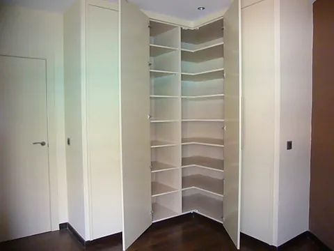 Una habitación con un armario esquinero con estantes y una puerta.