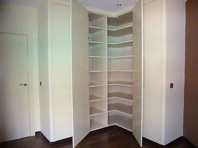 Una habitación con un armario esquinero con estantes y una puerta.