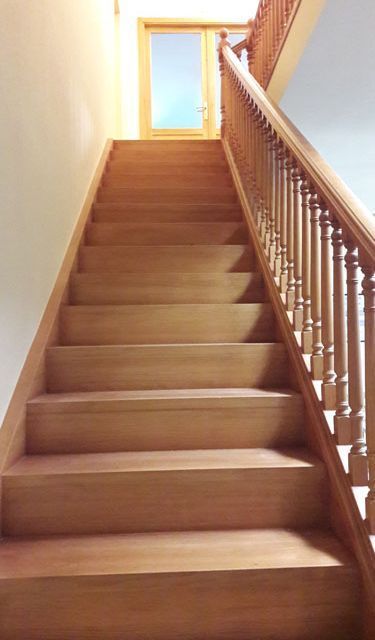 Una escalera de madera con una barandilla de madera que conduce a una puerta.