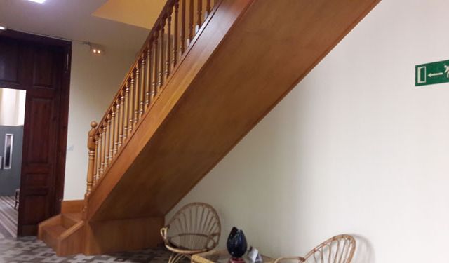 Una escalera de madera con una señal de salida verde en la pared.