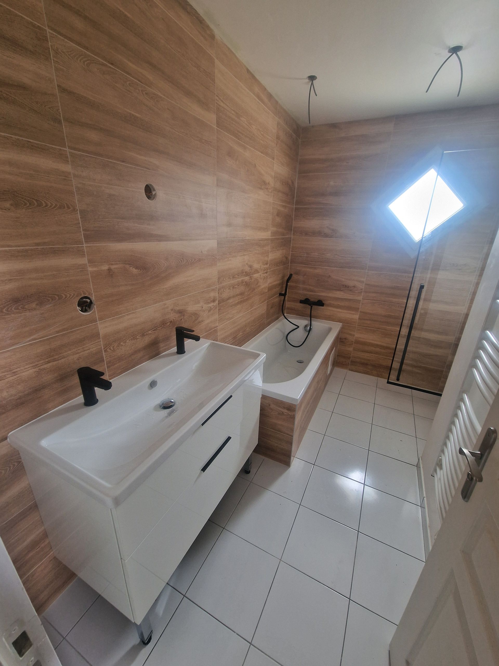 Salle de bains avec meuble-lavabo blanc, baignoire et murs carrelés marron. Fenêtre lumineuse et sol carrelé blanc.