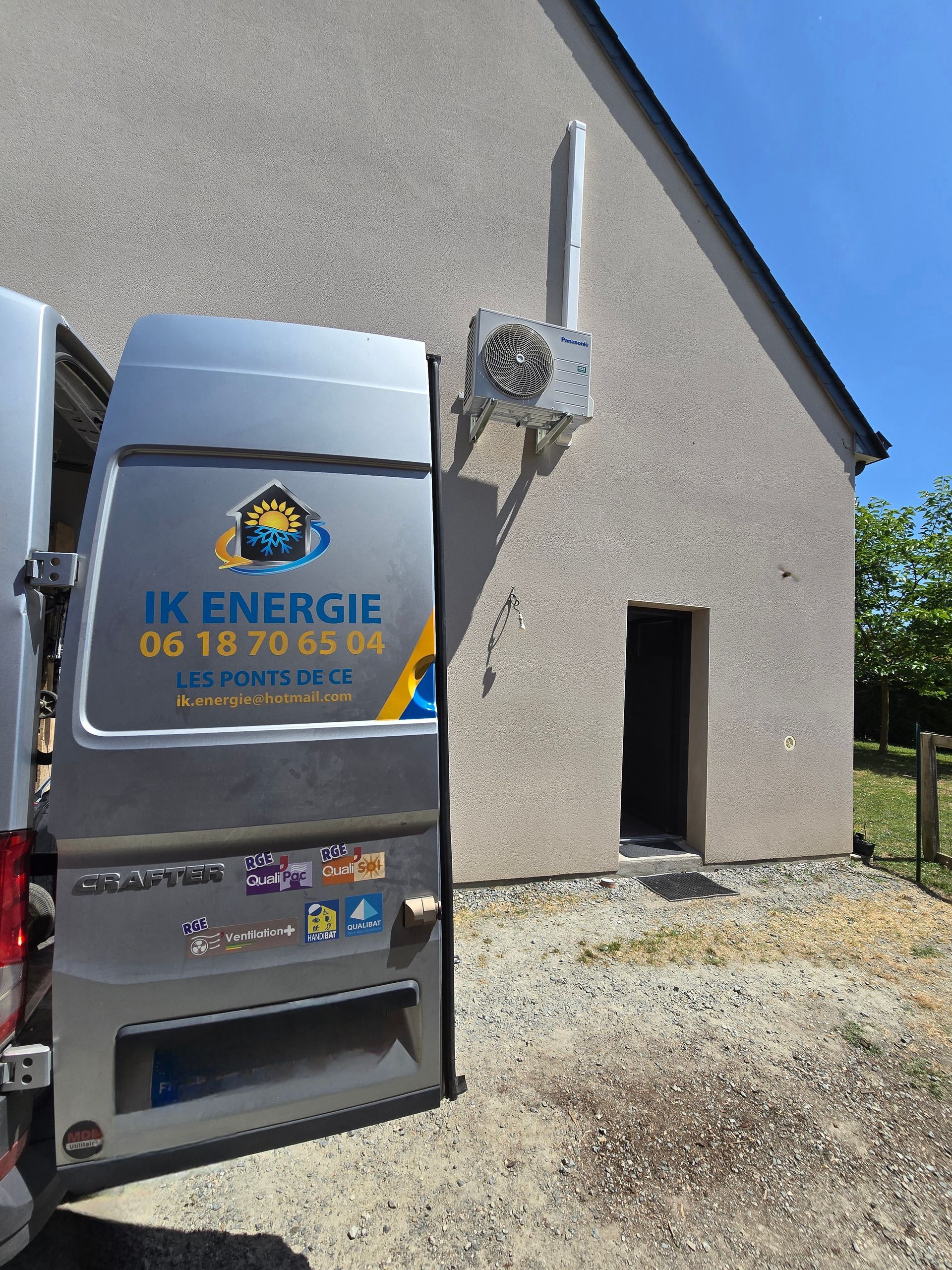 Une camionnette de service garée à côté d'un bâtiment avec une porte ouverte et un système de chauffage attenant, journée ensoleillée.
