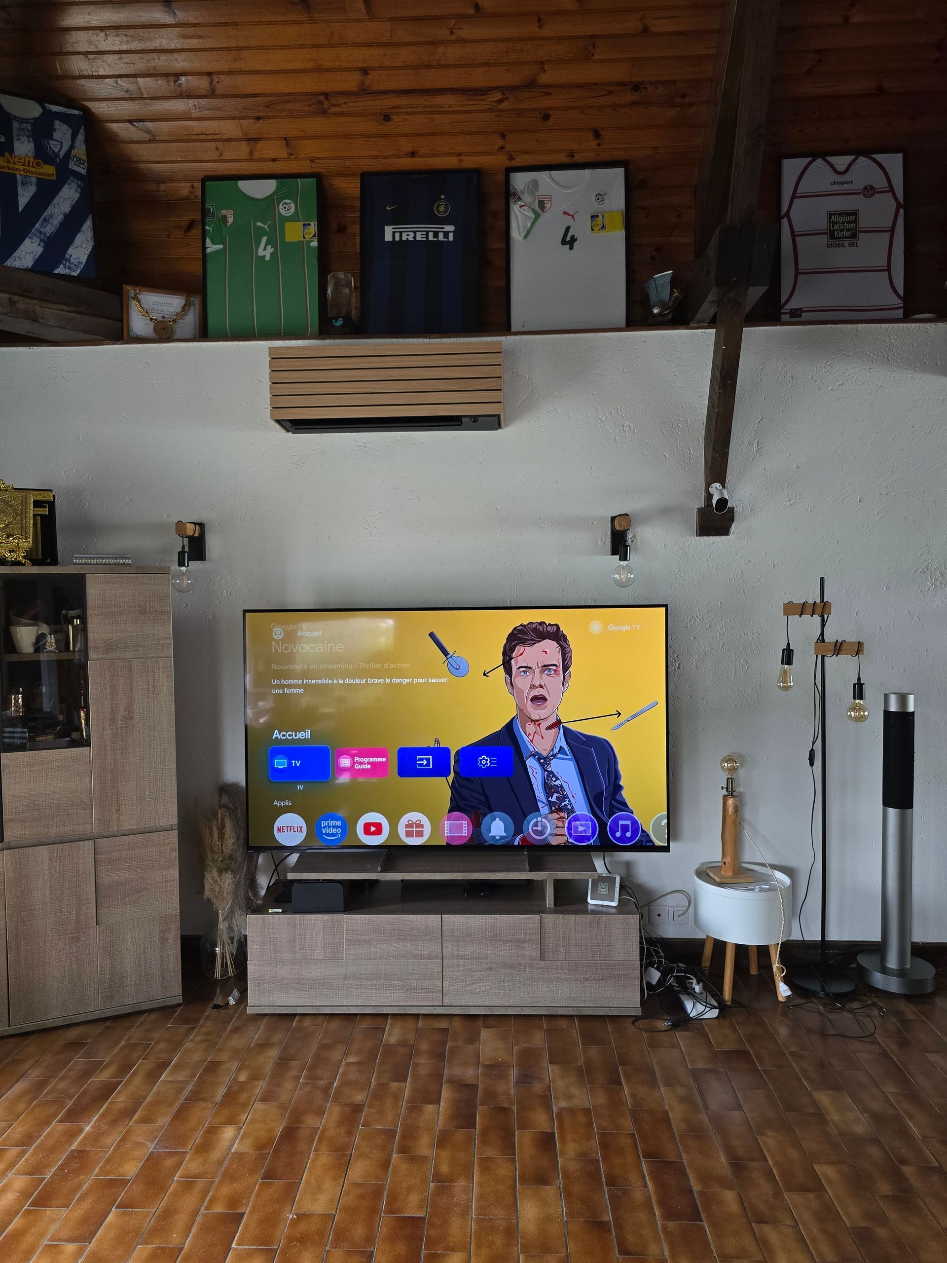 Séjour avec TV allumée, maillots encadrés, parquet et meubles intégrés.