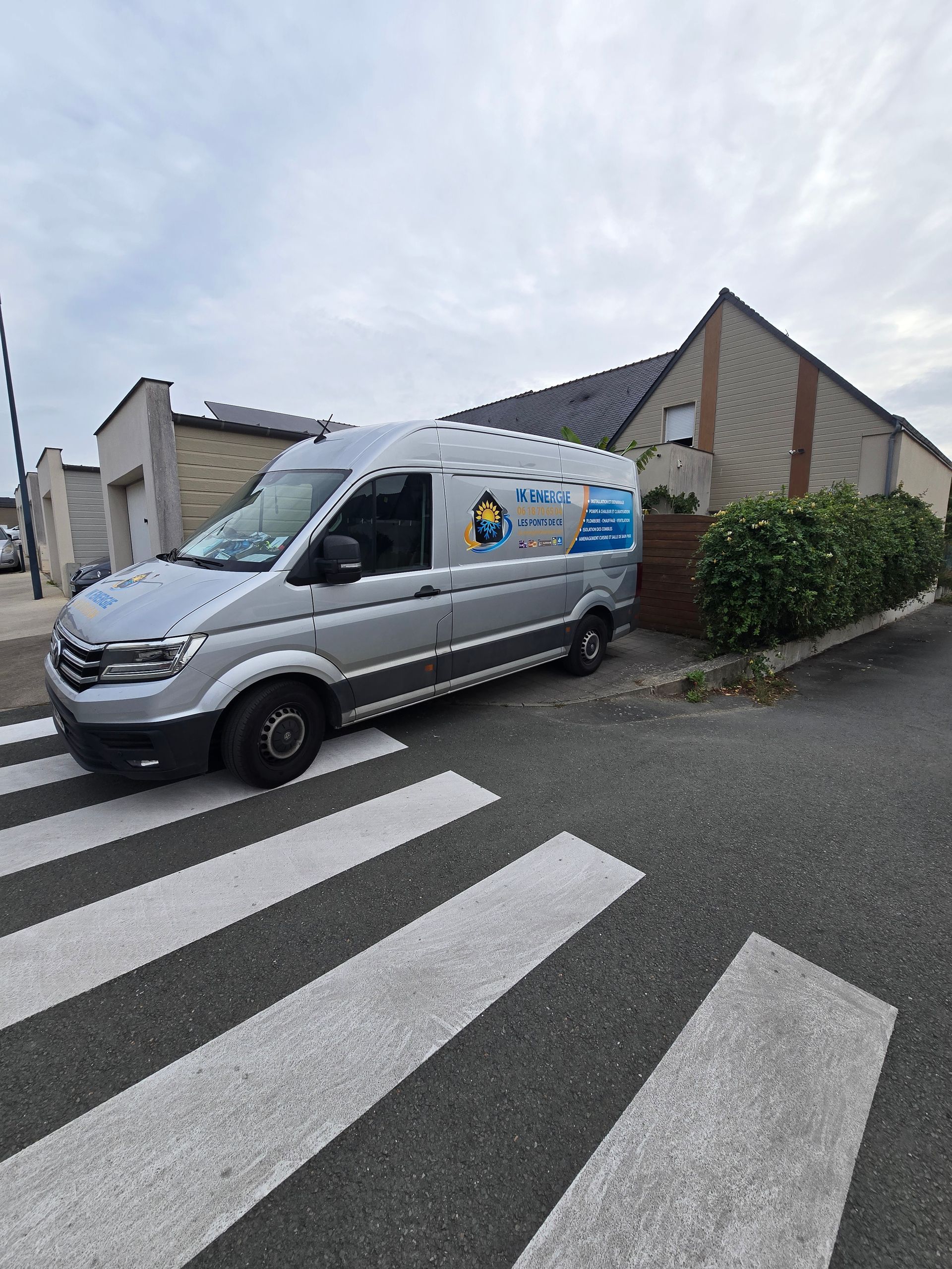 Fourgonnette argentée garée sur un passage piéton, à côté d'un immeuble résidentiel, par une journée nuageuse.