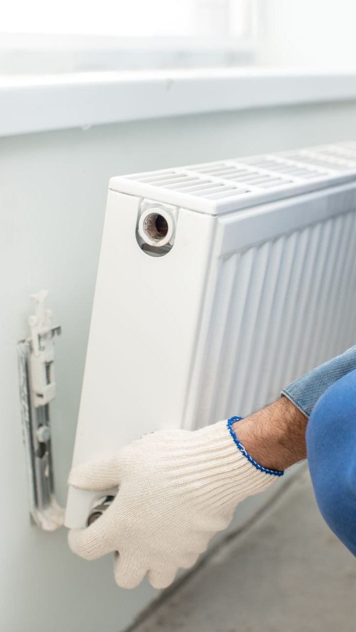 Une personne portant des gants installe un radiateur blanc sur un mur.