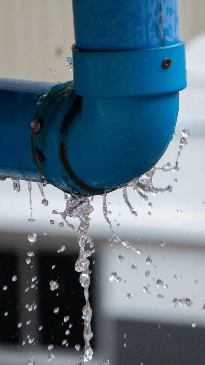 Coude de tuyau bleu qui fuit de l'eau, à l'extérieur.