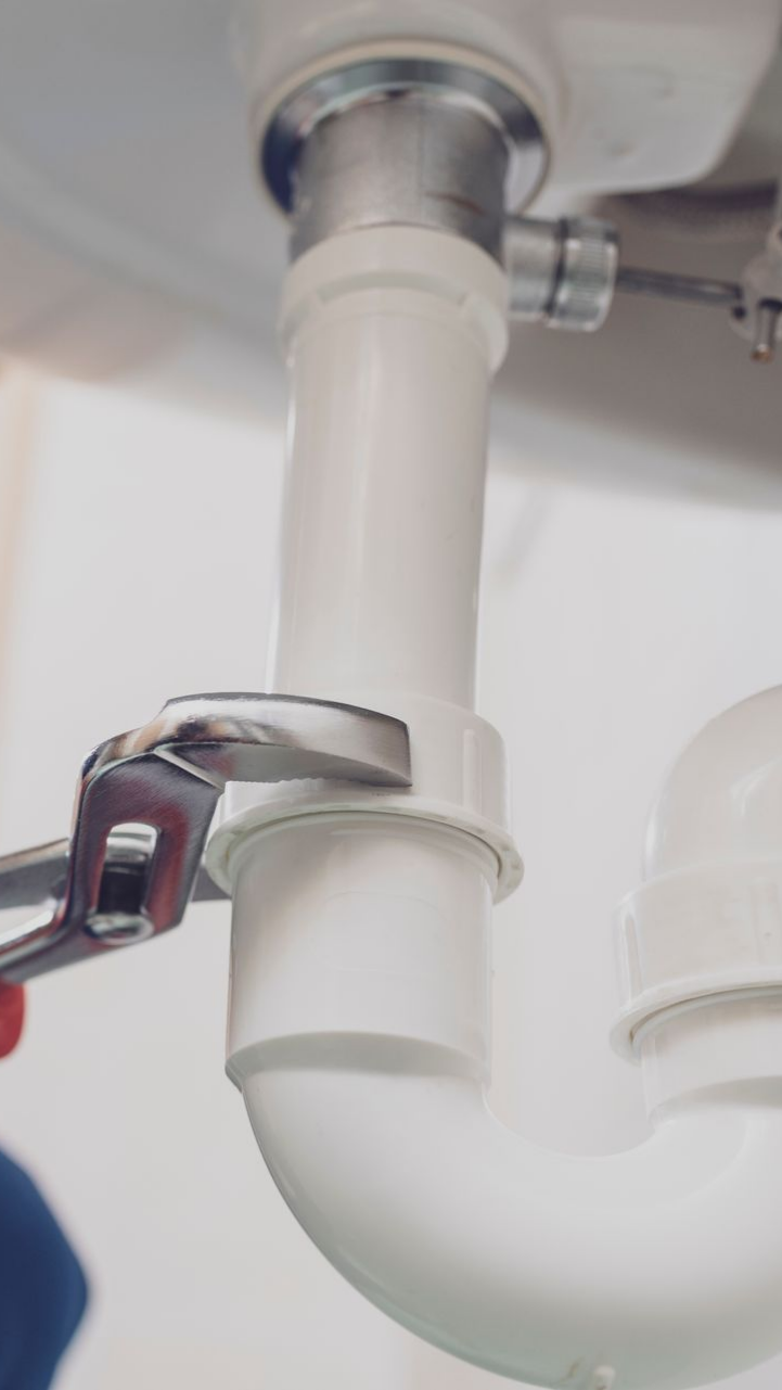 Une personne utilise une clé pour serrer un tuyau blanc sous un évier.