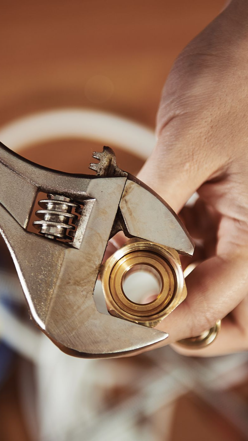 Main utilisant une clé pour serrer un raccord en laiton.