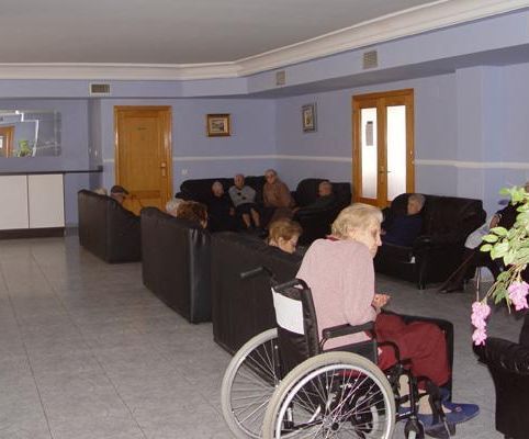 Una mujer en silla de ruedas se sienta en una sala de estar con otras personas.