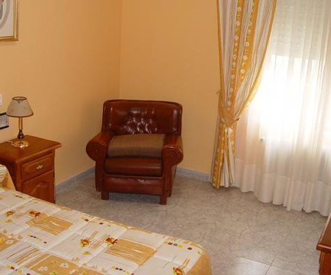 Un dormitorio con una cama, una silla y una ventana.