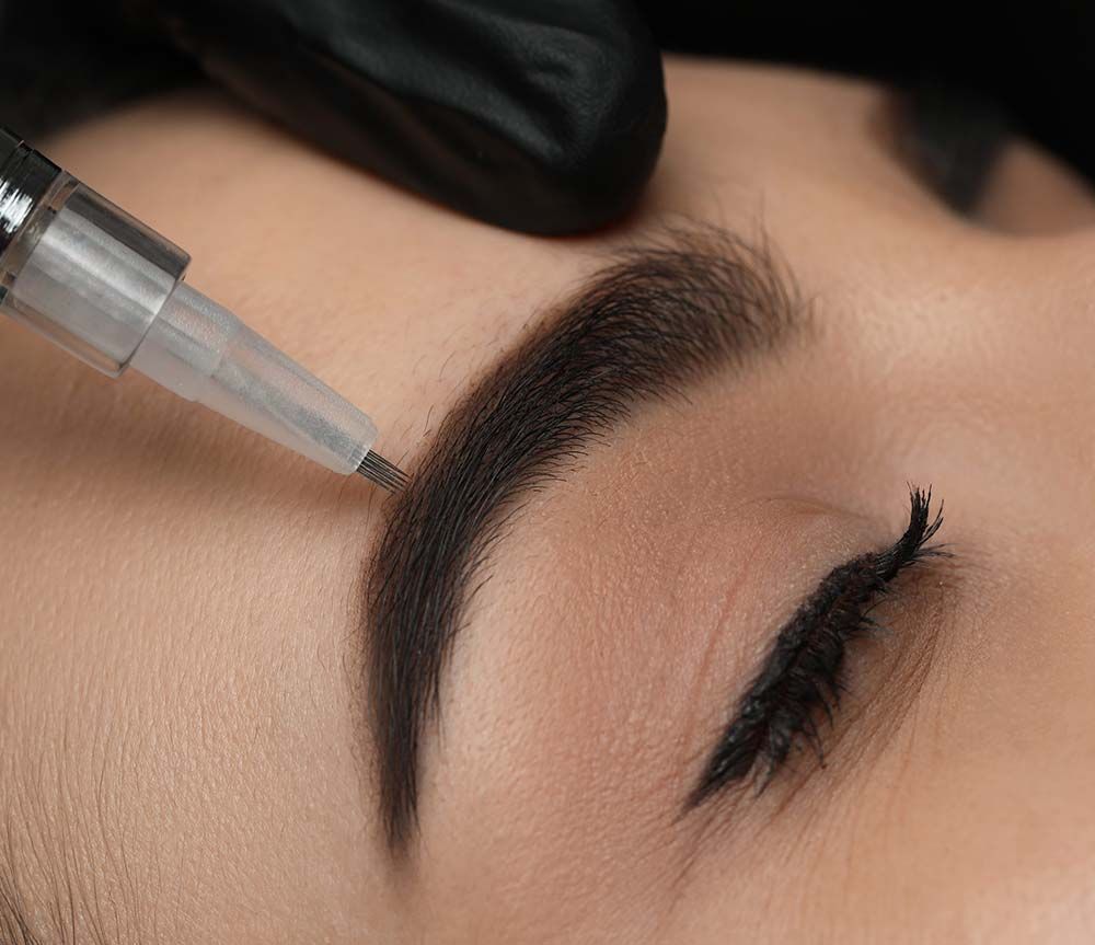 Primer plano de un procedimiento de tatuaje de cejas en el que una aguja manual define cuidadosamente la forma de la ceja.