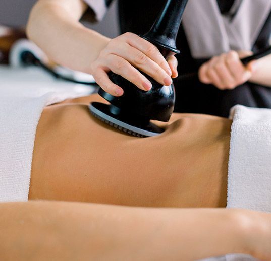 Durante un tratamiento de spa, un profesional utiliza un dispositivo de masaje de vacío manual de color negro en la zona abdominal de un cliente.