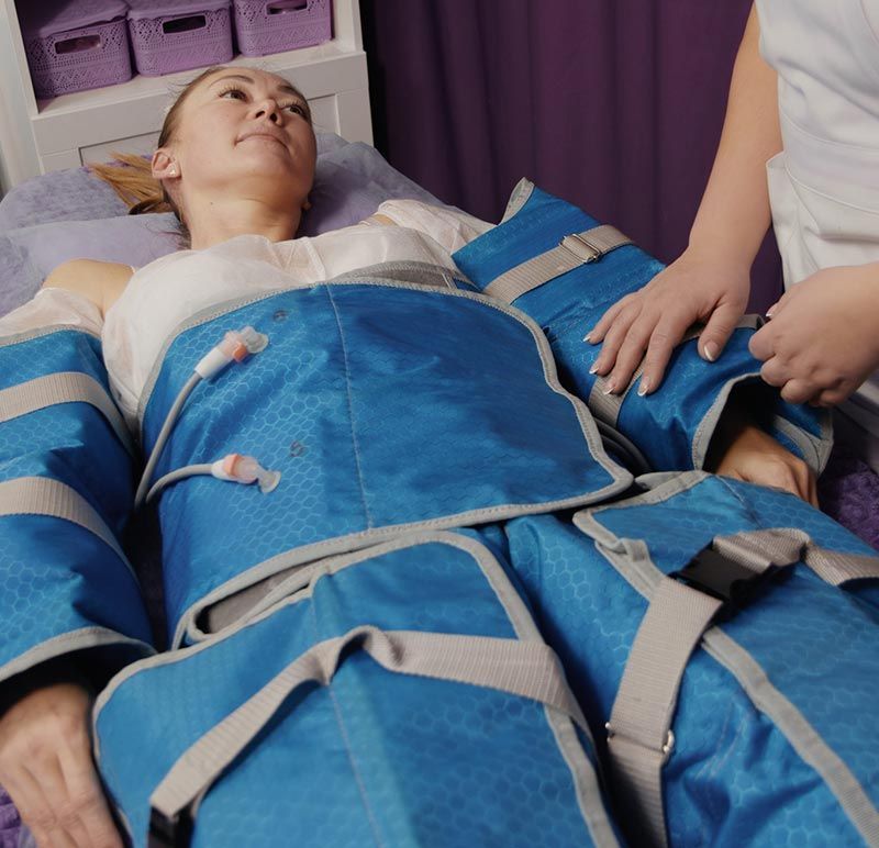 Una persona yace sobre una mesa, vestida con un traje de compresión azul de múltiples cámaras para un tratamiento terapéutico.