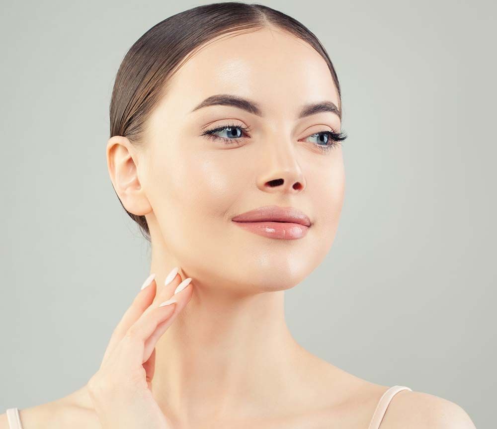 Una persona con la piel tersa y clara tocándose el cuello sobre un fondo gris claro.