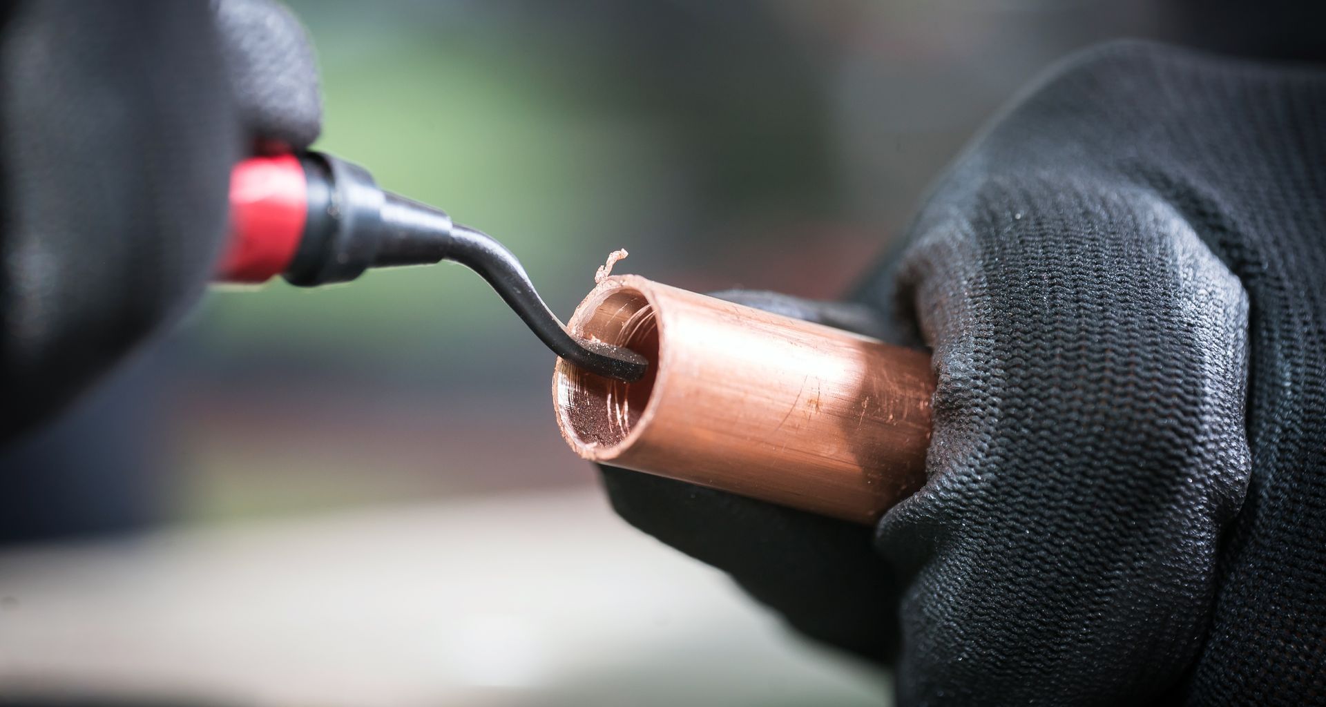 Des mains gantées de noir nettoient l'intérieur d'un tuyau de cuivre à l'aide d'un outil.