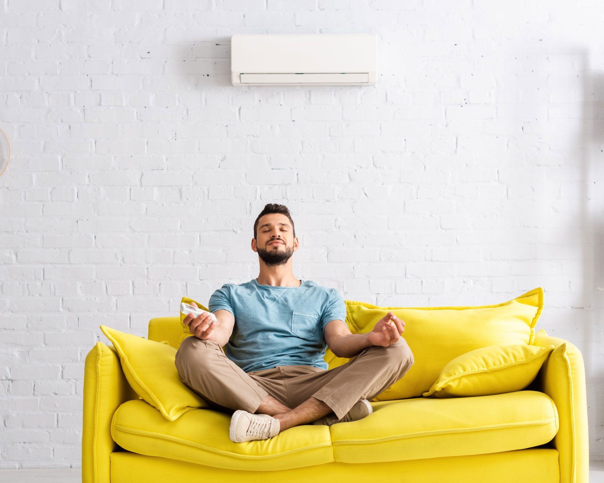 Un homme en position du lotus et l'air béat sur son canapé sous une climatisation