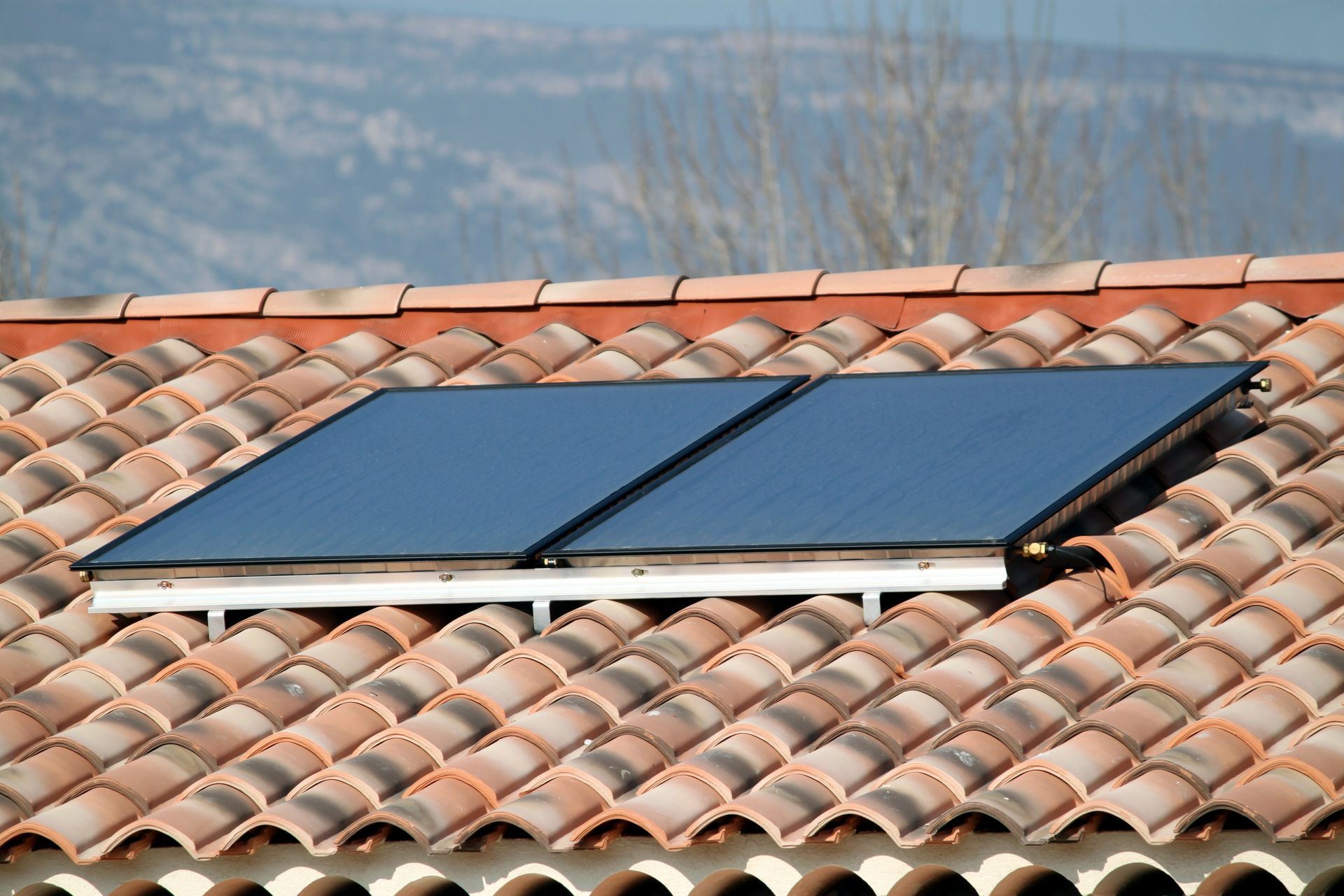 Deux panneaux solaires thermiques sur une toiture en tuiles dans un paysage de Provence