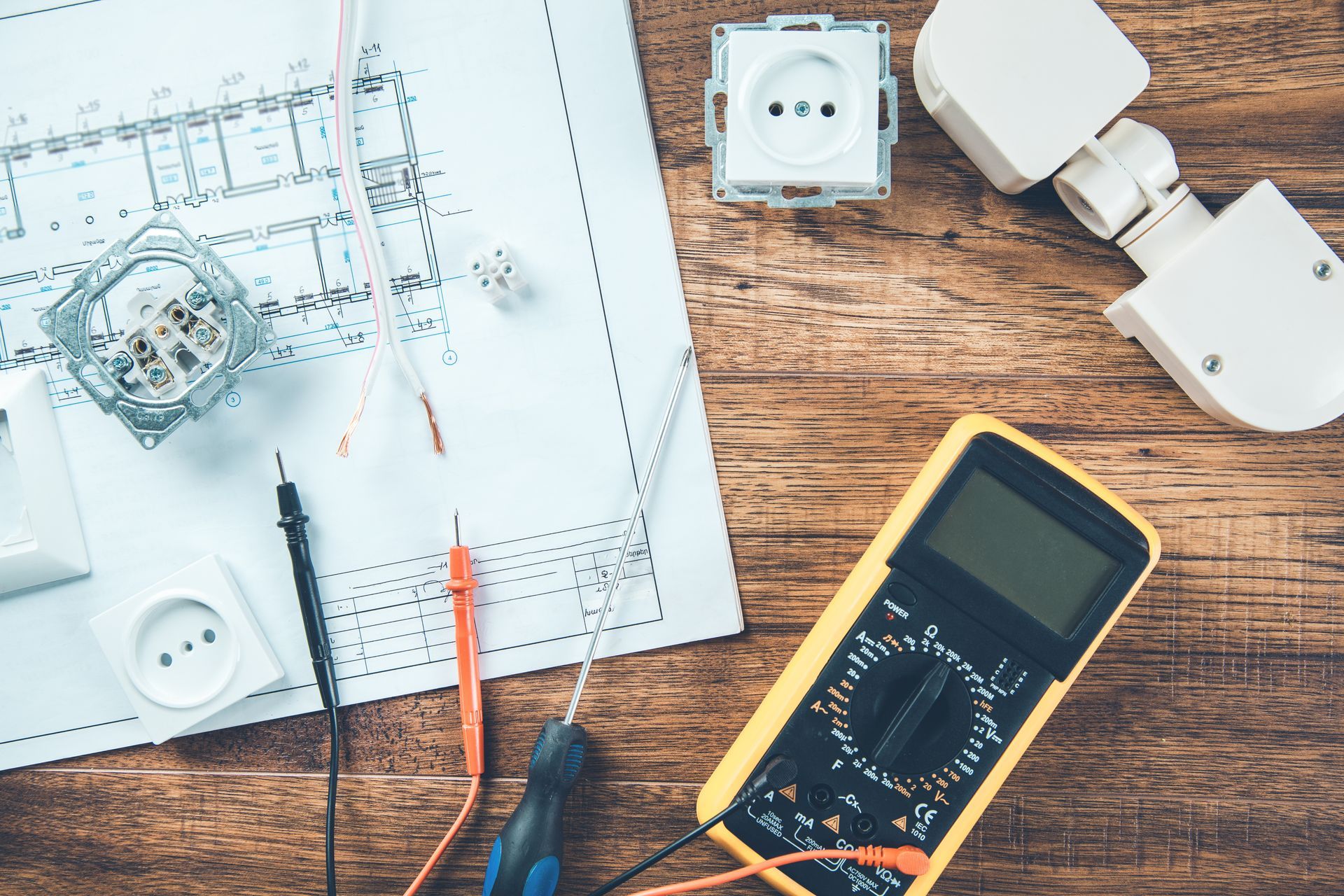 Des composants électriques, un multimètre, un tournevis et un plan d'étage disposés sur une table en bois.