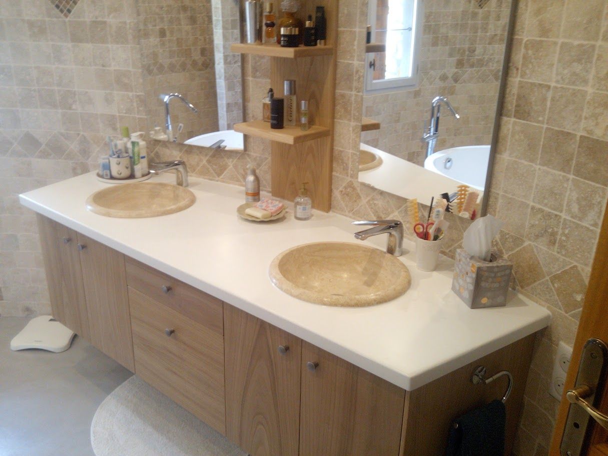 Un meuble-lavabo moderne à double vasque avec des armoires en bois clair, des vasques couleur pierre, un comptoir blanc et des murs carrelés.