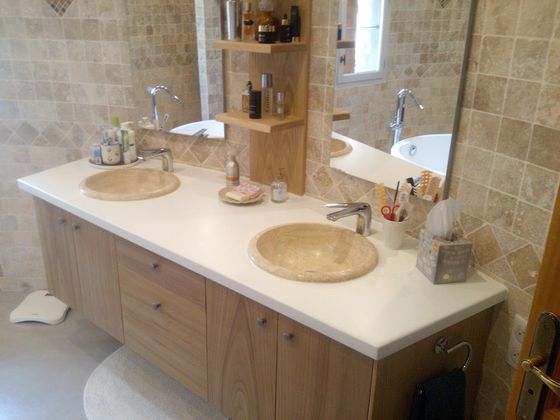 Un meuble-lavabo moderne à double vasque avec des armoires en bois clair, des vasques couleur pierre, un comptoir blanc et des murs carrelés.