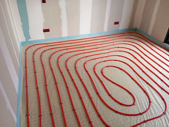 Tuyauterie PEX rouge pour chauffage au sol radiant, installée en grille sur le sol d'une pièce aux murs en plaques de plâtre non finies.