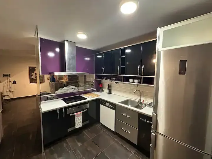 Cocina moderna con gabinetes negros, detalles en color púrpura, refrigerador de acero inoxidable y piso de baldosas.