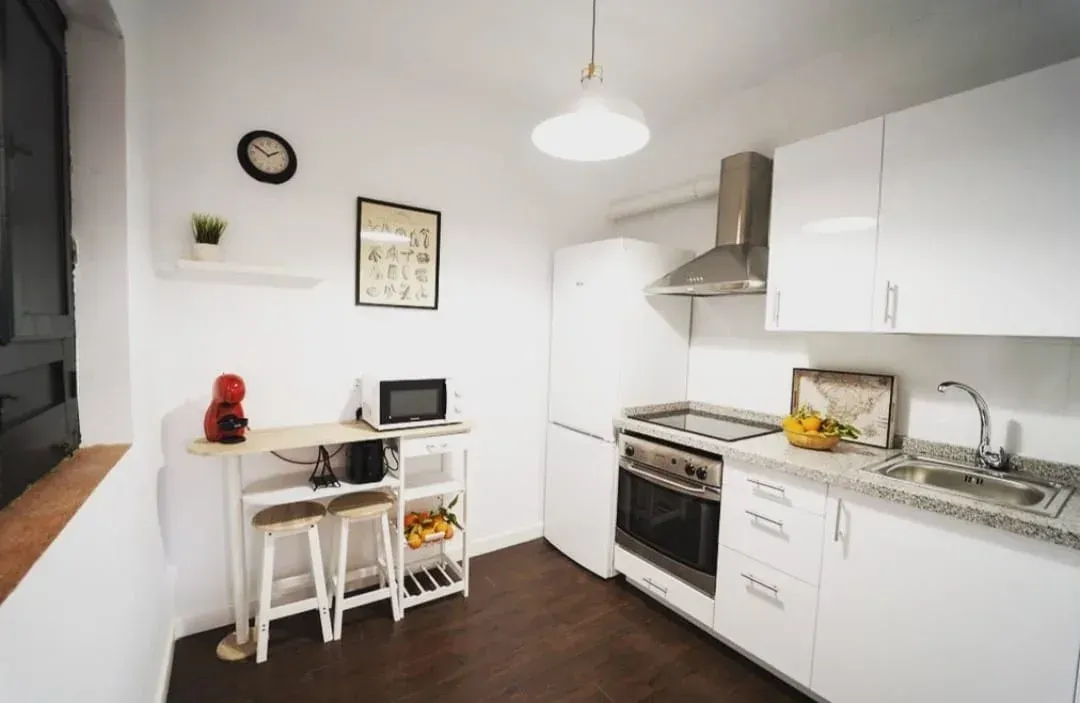 Cocina compacta de color blanco brillante con estufa, fregadero, refrigerador y un pequeño escritorio junto a la pared.