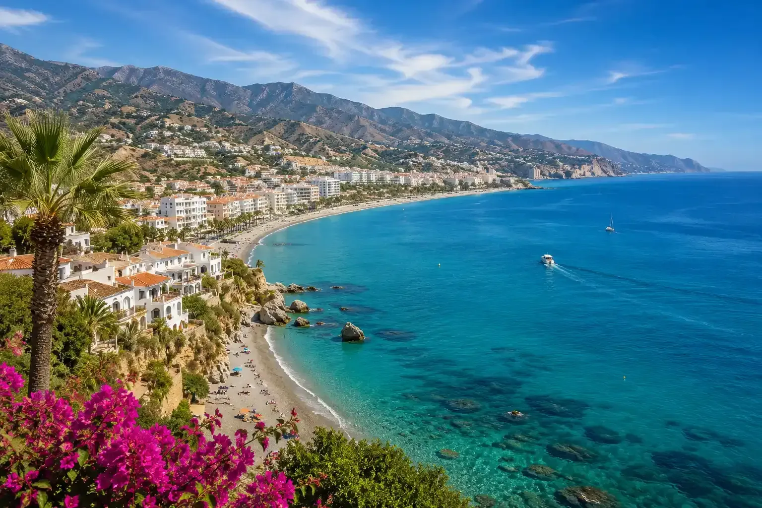 Pueblo costero soleado con bahía de color turquesa, playa de arena, casas en la ladera y flores rosas en primer plano.