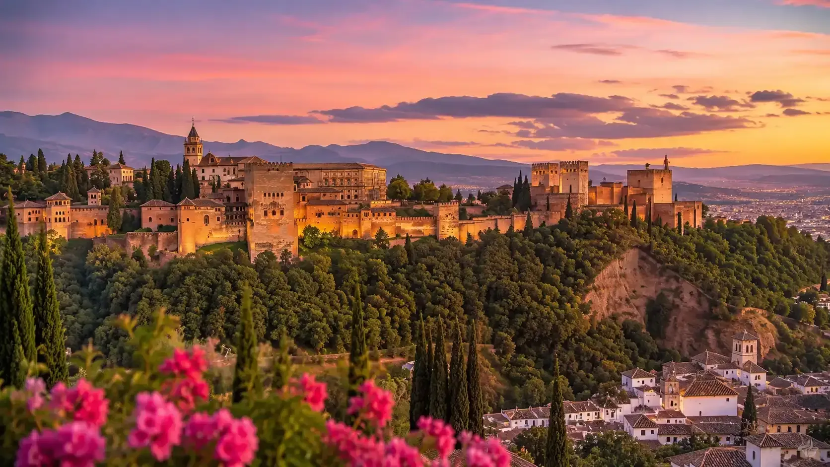 Puesta de sol sobre una fortaleza en la cima de una colina y el horizonte de la ciudad, con flores rosas en primer plano.