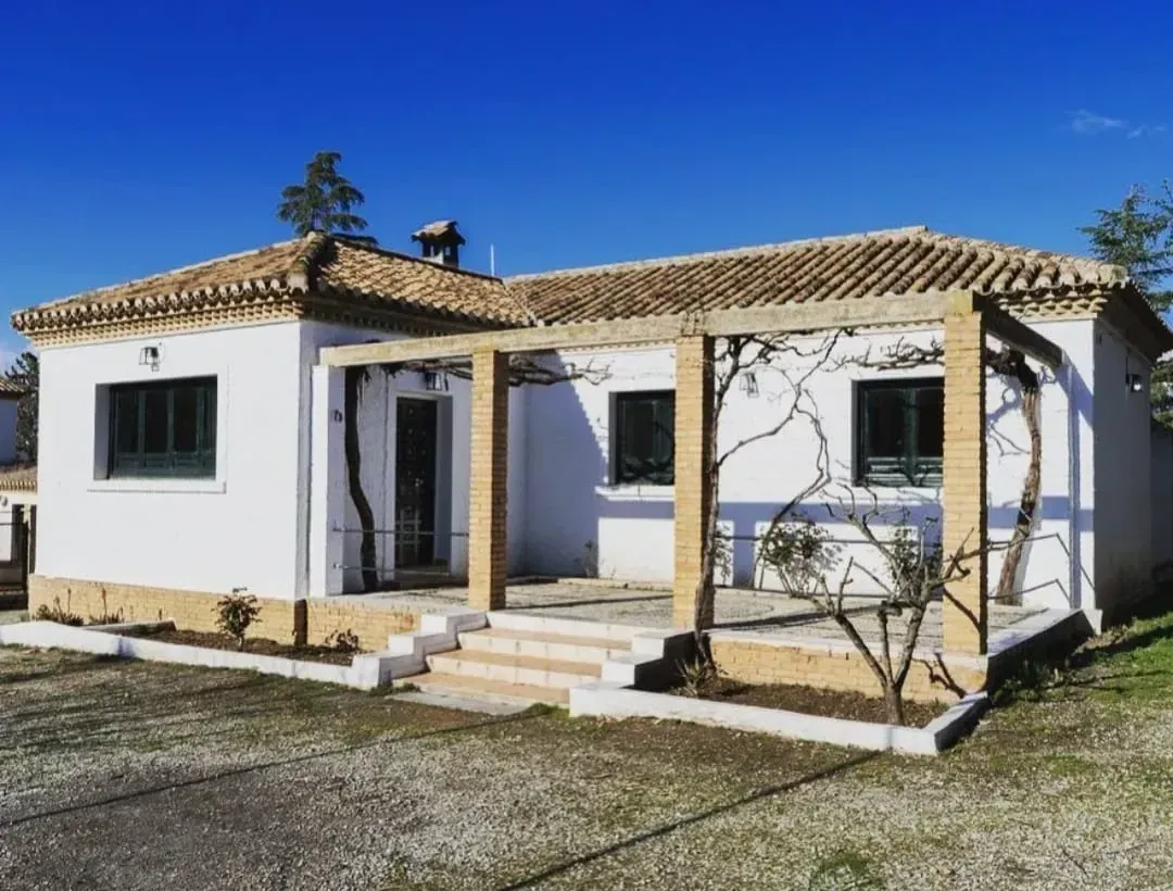 Casa blanca de una sola planta con techo de tejas, porche delantero y pequeño patio bajo un cielo azul despejado.