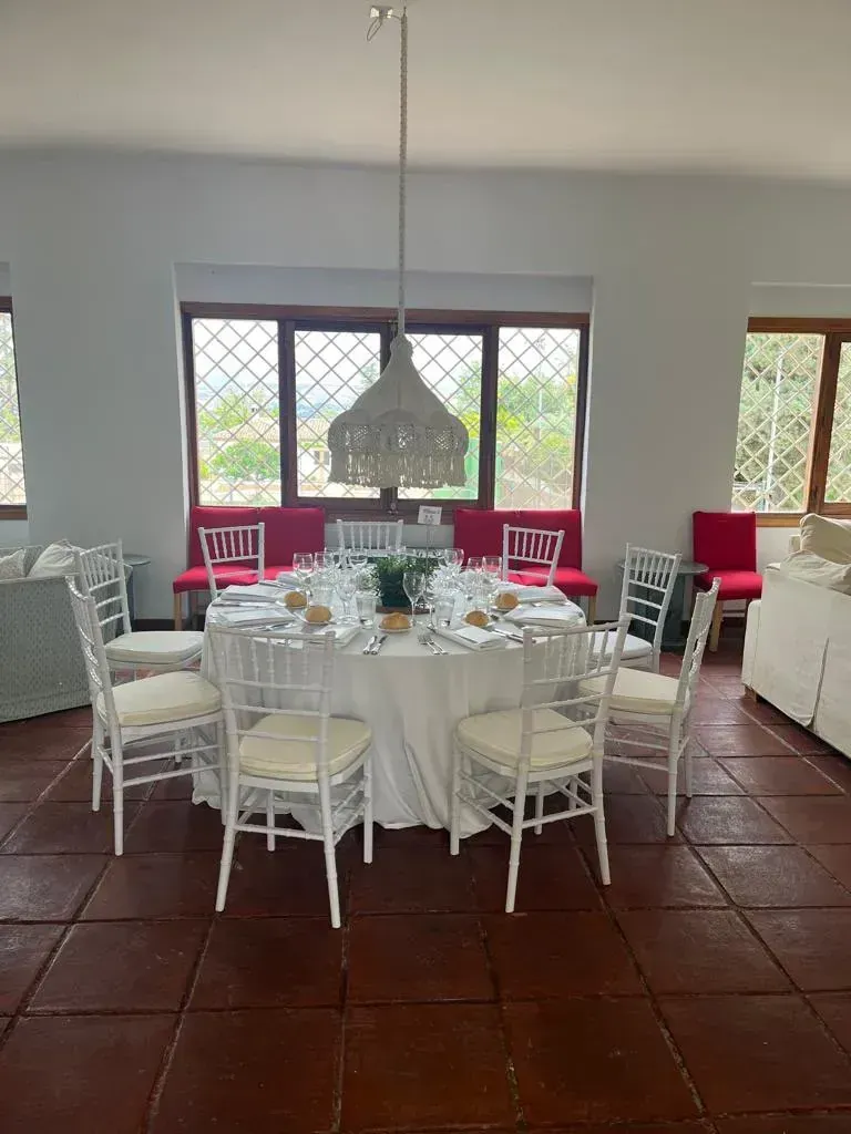 Mesa larga para banquetes bajo una carpa amarilla, con sillas blancas y centros de mesa florales