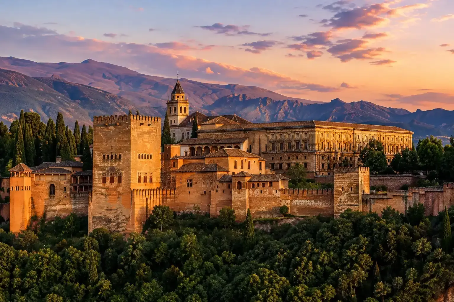 Puesta de sol sobre la fortaleza y el complejo palaciego de la Alhambra con las montañas al fondo.