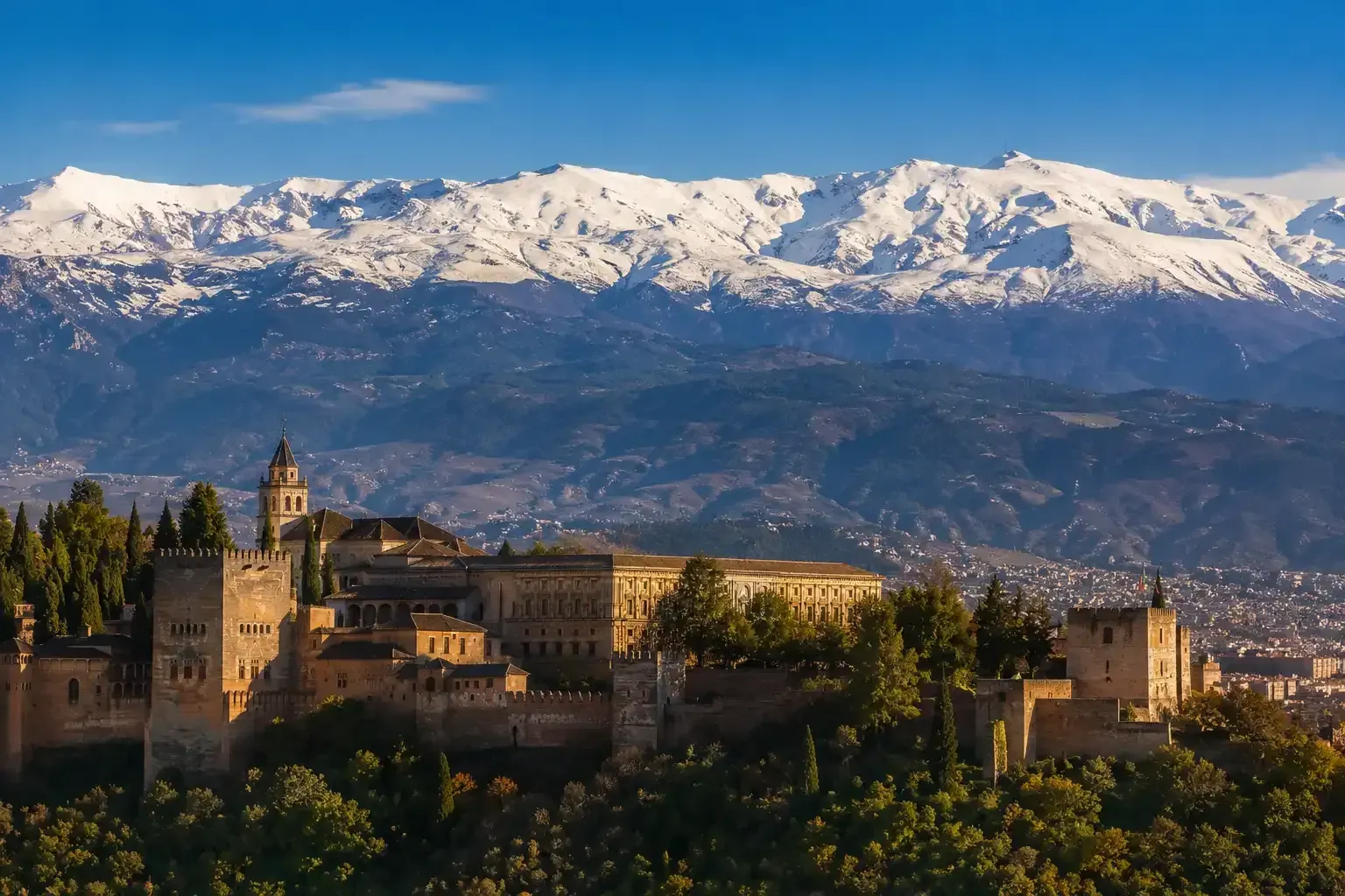 Montañas nevadas tras un histórico palacio en la cima de una colina al atardecer.