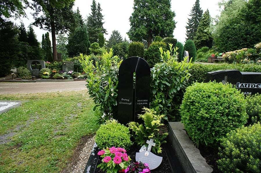 Ein Grab auf einem Friedhof mit Blumen und Büschen