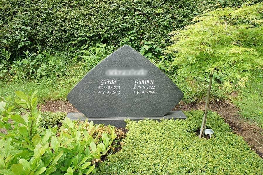 Ein Grabstein inmitten eines Gartens mit einem Baum im Hintergrund.