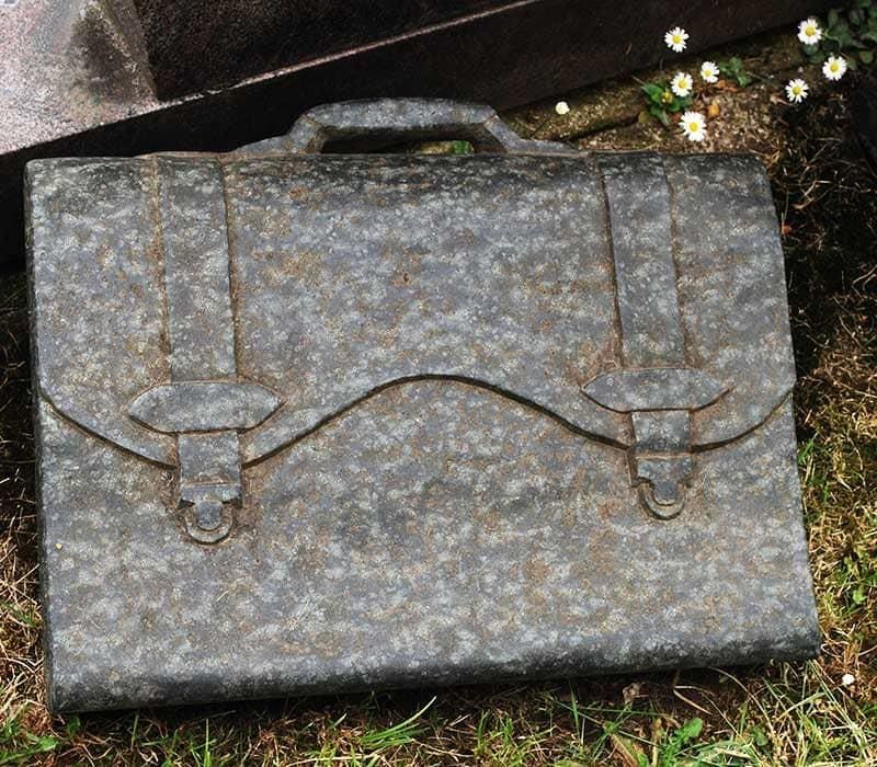 Eine Aktentasche liegt im Gras neben einem Grab