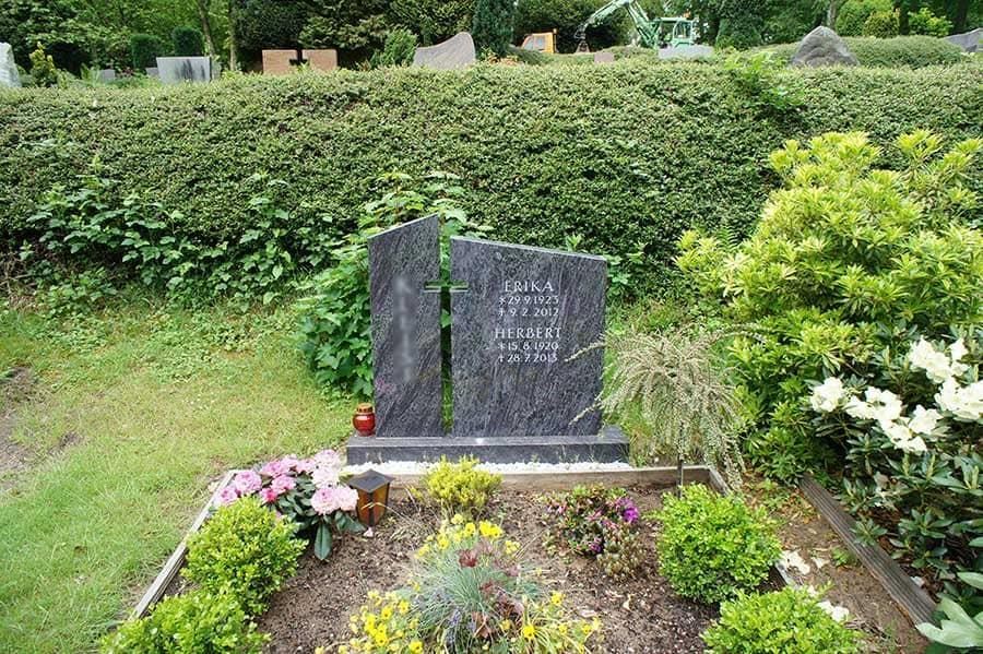 Ein Grab auf einem Friedhof, umgeben von Blumen und Büschen.