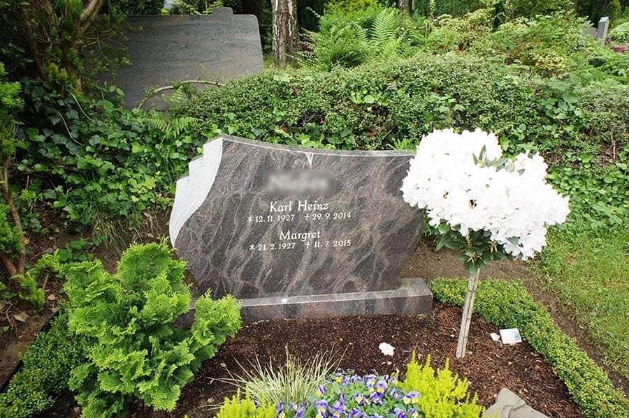 Ein Grab auf einem Friedhof mit Blumen und Büschen