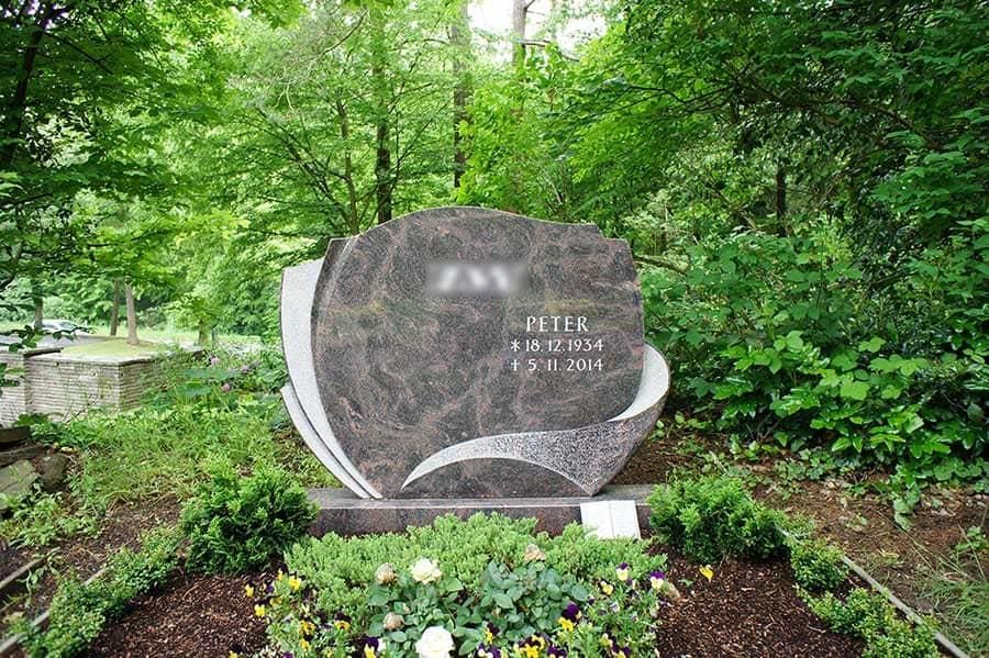 Ein Grabstein auf einem Friedhof, umgeben von Bäumen und Blumen.