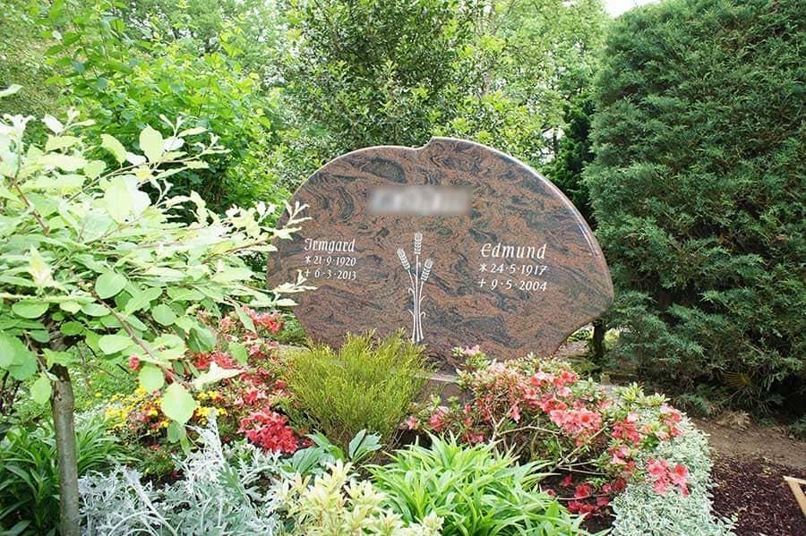 Ein Grabstein in einem Garten, umgeben von Blumen und Bäumen.