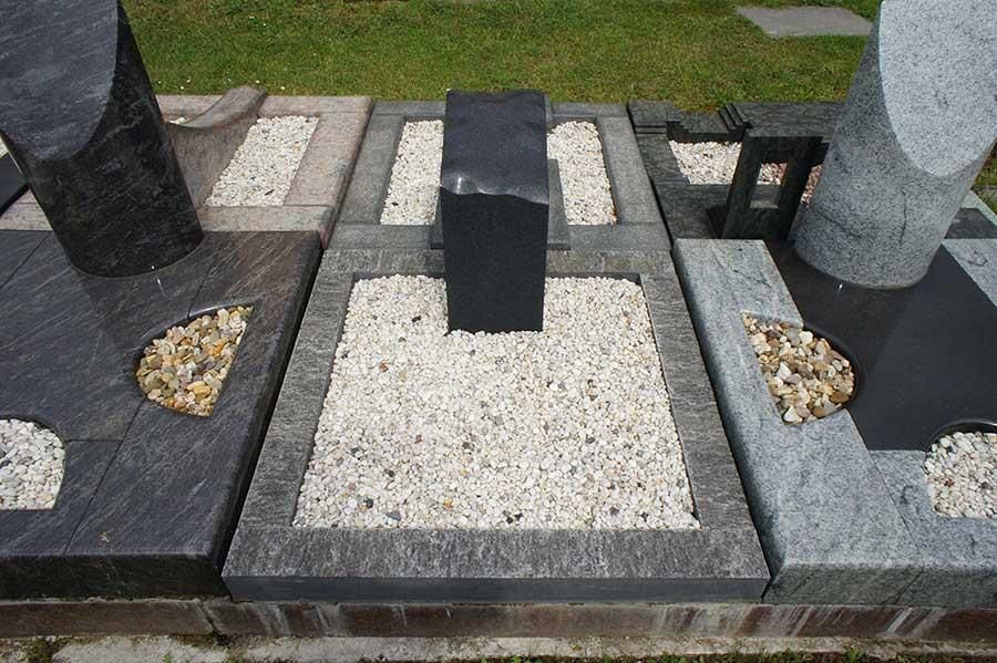 Eine Reihe von Gräbern mit Kies und einem schwarzen Würfel in der Mitte