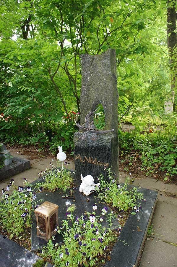 Ein Grab mit einer Vogelstatue darauf, umgeben von Blumen und Bäumen.