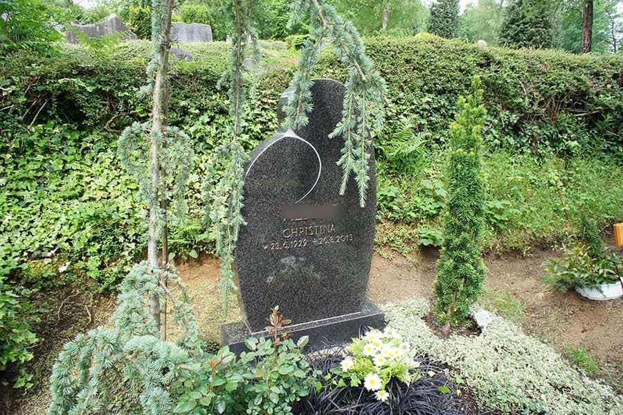 Ein Grabstein auf einem Friedhof, umgeben von Bäumen und Büschen.