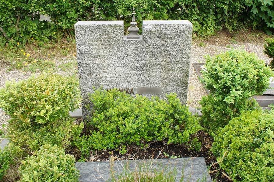 Ein Grabstein auf einem Friedhof, umgeben von Büschen und Sträuchern