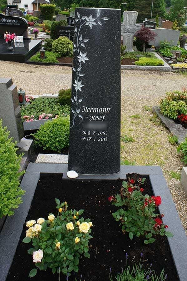 Ein Grab auf einem Friedhof mit Blumen und einem schwarzen Stein