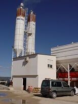 Una furgoneta está estacionada delante de un edificio con dos silos al fondo.