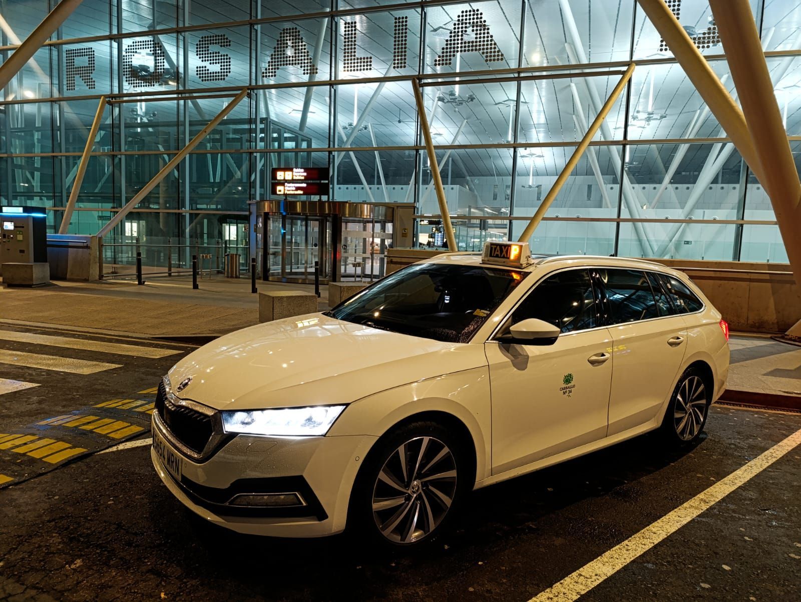 Un coche blanco está aparcado en un aparcamiento delante de un aeropuerto.