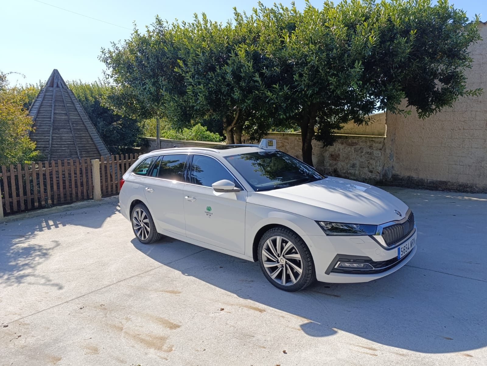 Un coche blanco está aparcado en un aparcamiento al lado de unos árboles.