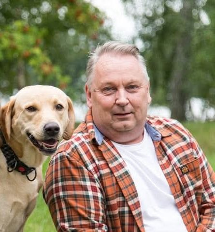 Ruutupaitainen mies keltaisen labradorinnoutajan kanssa ulkona vehreässä puistossa